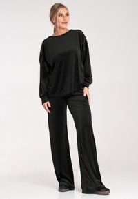 Czarny longsleeve i szerokie spodnie wykonane z gładkiego, miękkiego materiału. Całość ma luźny krój i minimalistyczny design.