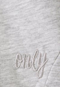 Tessuto grigio chiaro con una consistenza morbida, caratterizzato da un logo ricamato "only" in un filo grigio più chiaro, posizionato nell'angolo in basso a destra.