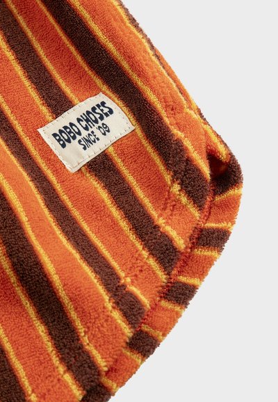 Serviette pliée avec des rayures orange, marron et jaune, comportant une étiquette blanche indiquant "BOBO CHOSES SINCE '09" sur un tissu texturé.