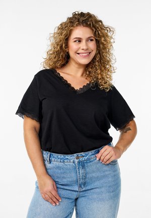 Schwarzes, kurzärmeliges Oberteil mit V-Ausschnitt, das mit Spitzenakzenten am Ausschnitt und an den Ärmeln verziert ist, getragen mit hellblauen, hochtaillierten Jeans.