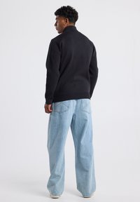 Black pullover with a high collar, made from soft material. Paired with light blue wide-leg jeans, showcasing a relaxed fit.