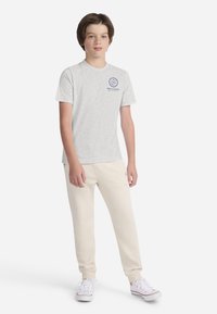 Maglietta di cotone grigia a maniche corte, con logo Abercrombie blu. Abbinata a pantaloni della tuta color crema e sneaker bianche.