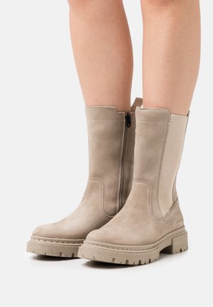 Beige enkellaarsjes van zacht suède met een paneel van gestructureerde stof, een ritssluiting aan de zijkant en een dikke rubberen zool. Heeft contrasterende stiksels langs de randen.