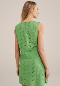 Rochie verde brodată, cu un design fără mâneci, un model floral din ochiuri și o deschidere în formă de cheie la spate. Lungime până la mijlocul coapsei și siluetă ajustată.
