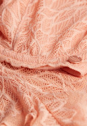 Lace fabric in soft peach hue with leaf pattern, featuring a round metal tag with engraving. Textured, lightweight, and delicate finish.