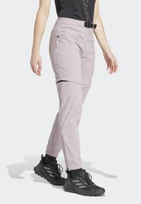 Person wearing light purple zip-off pants with black belt and black athletic shoes, standing against a plain light background.