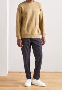 Sweat-shirt marron avec le texte "Copenhagen", associé à un pantalon foncé effilé et des baskets blanches. Tissu lisse, design simple, coupe décontractée.