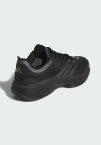 Chaussure de sport noire avec un dessus en maille, des accents texturés et trois rayures foncées. Elle dispose d'une semelle rembourrée et d'un col rembourré pour un meilleur soutien.
