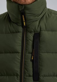 Puffer jacket in dark green, featuring quilted texture. Black zipper with yellow logo detail and high collar for added warmth.