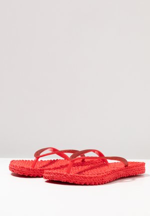 Pair of red woven flip-flops with textured soles and thin glittery straps on a white surface against a neutral background.