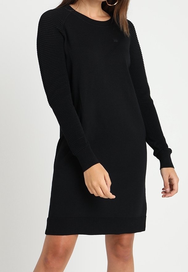 Svart långärmad klänning med ribbat mönster på ärmarna, rund halsringning och en solid kropp. Skräddarsydd passform med stickad kvalitet.