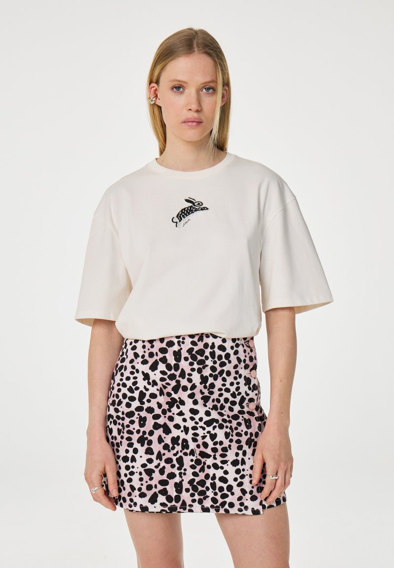 Crème katoenen T-shirt met een zwart geborduurd konijngrafiek, gecombineerd met een roze minirok met een zwart gespikkeld patroon.