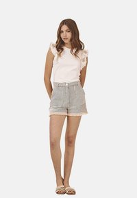 Top blanco sin mangas con hombros con volantes, combinado con pantalones cortos a cuadros con dobladillo deshilachado. Se lleva con sandalias ligeras.