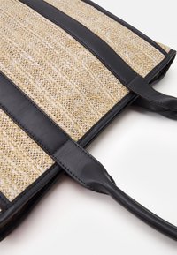 Tkaná slaměná taška s černými koženými akcenty. Obsahuje texturovaný, vzorovaný povrch a dvojité pevné rukojeti pro snadné nošení.