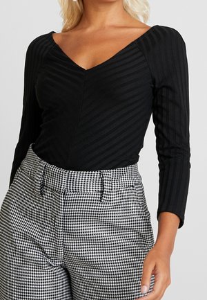 Sort ribbet bluse med lange ærmer og V-hals, kombineret med højttaljede bukser i sort og hvidt hundetandsmønster.