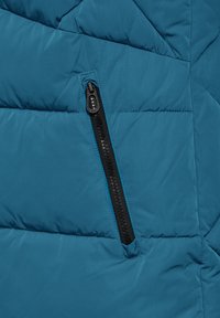 Teal puff jacka med diamantquiltat mönster, med en svart dragkedjeficka och slät, glänsande yta.