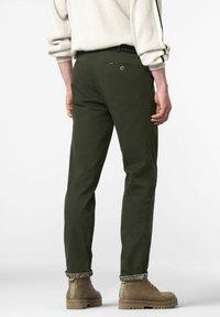 Olivgrüne Chinos mit geradem Schnitt, ausgestattet mit Gesäßtaschen, dezenten Texturen und gemusterten Cuffs. Dazu beigefügt sind beigefarbene Stiefeletten.