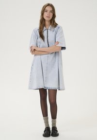 Robe en jean bleu clair avec un col, des manches courtes et une coupe ample. Elle est dotée de poches latérales et d'un ourlet droit.