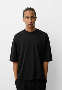 Tricou scurt negru, din bumbac moale, cu o croială lejeră și guler rotund, fără logo-uri sau modele vizibile.