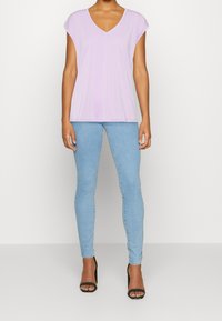 Ljuslila kortärmad V-ringad topp kombinerad med ljusblå skinnyjeans och svarta sandaler med öppen tå, vilket ger en avslappnad passform.