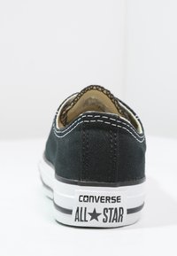 Svarte lær-sko med lavt design, hvit gummisåle og kontrastsøm. Har "Converse All Star"-merke på hælen.