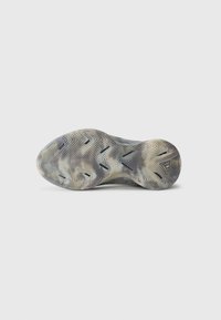 Semelle de chaussure de sport en caoutchouc avec un motif en chevrons, présentant un mélange de tons gris et beige, une surface texturée et des lignes de semelle distinctes.
