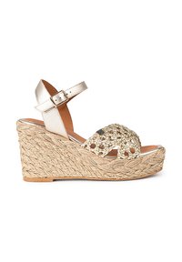 Sandale à talon en jute tressé et or métallique, avec des accents tissés décoratifs et une bride ajustable à la cheville. La semelle présente une finition texturée.