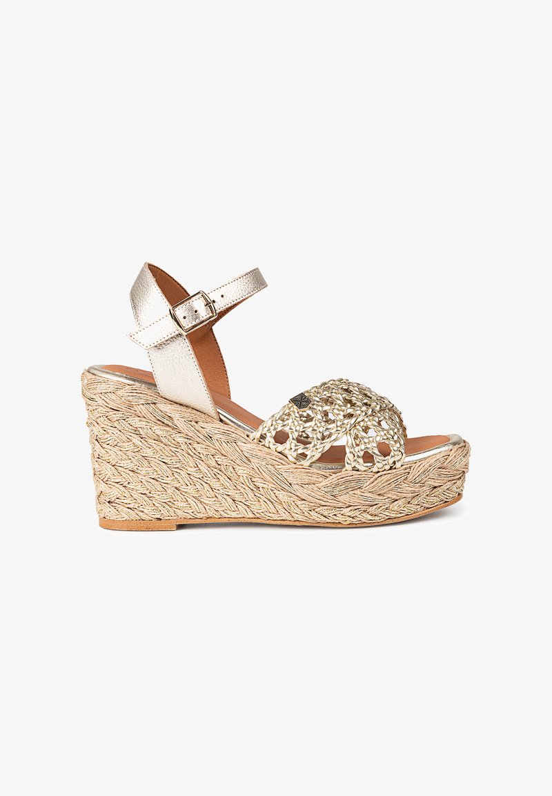 Sandale à talon en jute tressé et or métallique, avec des accents tissés décoratifs et une bride ajustable à la cheville. La semelle présente une finition texturée.