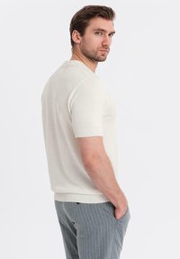 Lys beige kortærmet strikket polo skjorte med en tekstureret overflade, ribbet krave og manchetter, parret med grå stribede bukser.