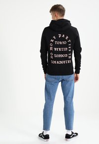 Zwarte hoodie met een grote roze print op de achterkant, met stadsnamen: Tokio, Berlijn, Londen, Los Angeles. Katoen-spandexmix, casual pasvorm.