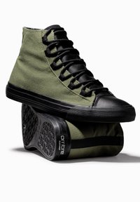 Baskets montantes en toile vert olive avec des accents noirs et une semelle en caoutchouc. Dotées d'une semelle extérieure texturée et de lacets noirs. Design remarquable à bout rond.