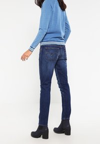 Mörkblå denimjeans med slim fit och sydda bakfickor, kombinerat med en ljusblå tröja och svarta klackboots.