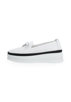 Biały sneaker typu slip-on z perforowanym wzorem, czarną lamówką wokół podeszwy, grubą białą platformą oraz małym dekoracyjnym metalowym detalem na wierzchu.