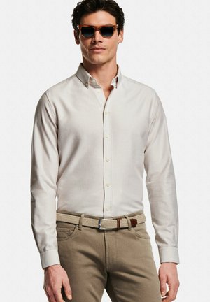 Lichtgekleurd, gestreept overhemd met knopen en een kraag, gecombineerd met een geweven riem en beige broek. Model draagt een zonnebril.