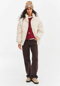 Prošívaná bunda v krémově bílé barvě, texturovaná látka; pod ní bordó svetr; hnědé manšestrové kalhoty; béžové boty s růžovými šňůrkami; opálená čepice.