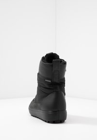 Bottine noire à cheville avec une tige texturée, un talon en cuir lisse et une languette de tirage. Présente un logo Gore-Tex imperméable sur le côté.