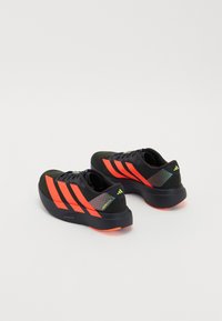 Des chaussures de sport avec un dessus noir, des rayures rouges et des accents verts. Elles disposent d'une semelle rembourrée et d'un talon texturé pour le soutien.
