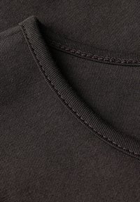 Tissu en coton marron foncé présentant un col rond et une texture à fines côtes. Les coutures sont visibles le long des bords, offrant une finition soignée.