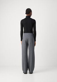 Pantalons larges gris en tissu texturé et taille haute, associés à un turtleneck noir ajusté à manches longues. Vue de dos.