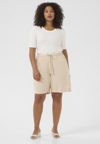 Beige shorts with a drawstring waist and side pockets, paired with a fitted, white ribbed t-shirt and off-white heeled sandals.