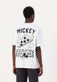 White cotton t-shirt featuring a black graphic design on the back with a pizza slice, Mickey Mouse, and text elements in bold lettering.