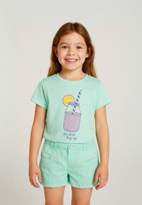 T-shirt vert menthe avec un graphique d'une boisson dans un bocal mason, mettant en vedette une rondelle de citron et une paille. Associé avec un short assorti vert menthe.