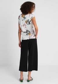 Szary top w kwiatowy wzór z krótkimi rękawami, zestawiony z czarnymi spodniami o szerokich nogawkach i zielonymi sandałami na obcasie. Gładka tekstura i luźny krój.