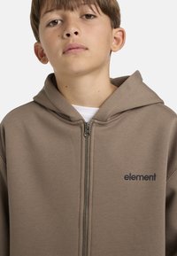 Felpa con zip marrone con finitura testurizzata e cappuccio, caratterizzata da un piccolo logo "element" nero sul lato sinistro. Vestibilità standard con una zip liscia.