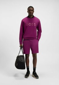 Purple sweatshirt with embossed "BOSS" logo, matching purple shorts, black sneakers, and a black bag. Smooth fabric, casual fit.