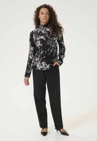 Blusa nera a fiori con maniche lunghe, caratterizzata da un collo alto e un tessuto morbido. Abbinata a pantaloni neri sartoriali e tacchi neri a punta.