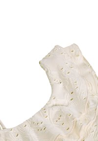 Λευκό ύφασμα με περίπλοκο λουλουδάτο κέντημα και λεπτομέρειες από δαντέλα που σχηματίζουν μια ρυτιδωτή άκρη σε ένα ρούχο.