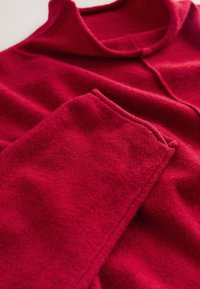 Pull rouge doux avec un col montant et des manches longues posé à plat, mettant en valeur la texture du tissu et les détails des coutures.