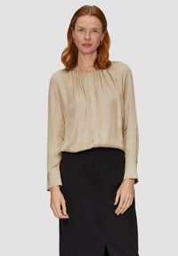 Beige blouse met lange mouwen van een gladde stof, met een gathered halslijn en subtiele plooien, gecombineerd met een zwarte rok met een zijsplit.