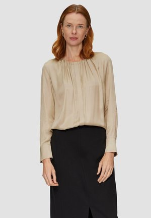 Blusa beige a maniche lunghe in tessuto morbido con scollatura arr gathered e pieghe sottili, abbinata a una gonna nera con spacchi laterali.